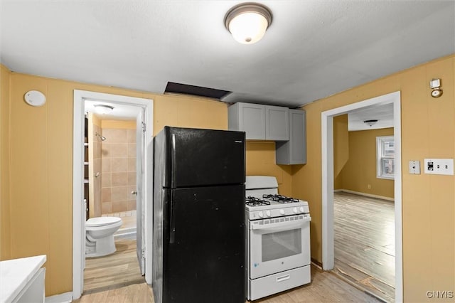 kitchen with black refrigerator, white gas stove, gray cabinets, and light wood-type flooring