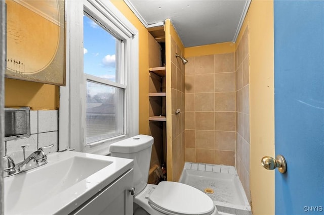 bathroom featuring toilet, vanity, tiled shower, and ornamental molding