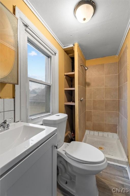 bathroom with toilet, vanity, backsplash, ornamental molding, and a tile shower