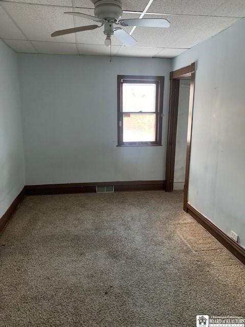 carpeted empty room featuring ceiling fan and a drop ceiling