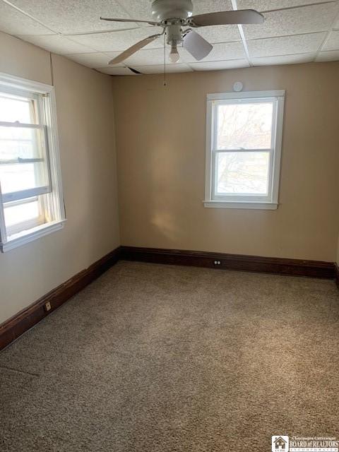 unfurnished room with ceiling fan, carpet flooring, and a drop ceiling