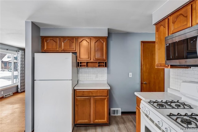 kitchen with tasteful backsplash, white appliances, and light hardwood / wood-style flooring