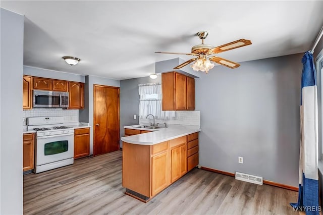 kitchen with light hardwood / wood-style floors, kitchen peninsula, tasteful backsplash, white gas stove, and sink