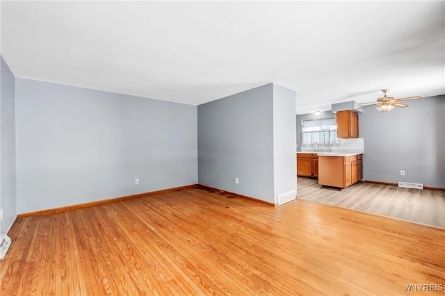 unfurnished living room featuring ceiling fan, sink, and light wood-type flooring