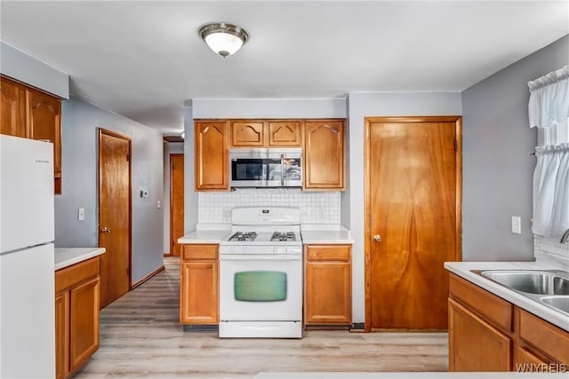 kitchen with light wood-type flooring, sink, backsplash, and white appliances