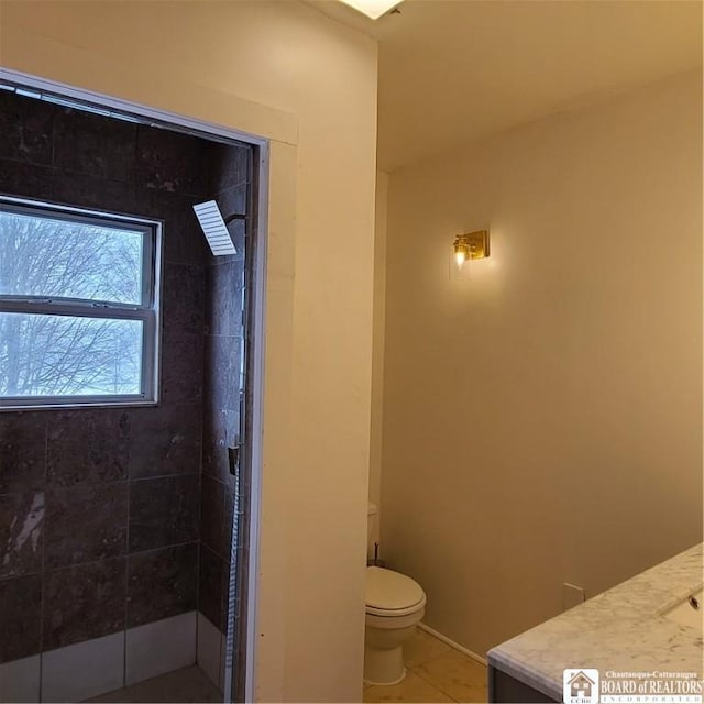 bathroom featuring toilet, vanity, tile patterned floors, and tiled shower