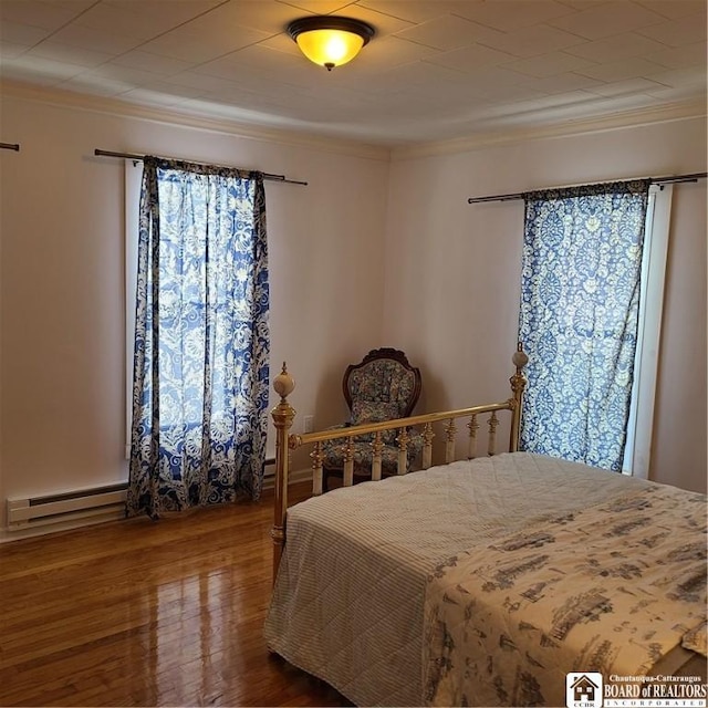 bedroom featuring a baseboard heating unit, hardwood / wood-style floors, and multiple windows