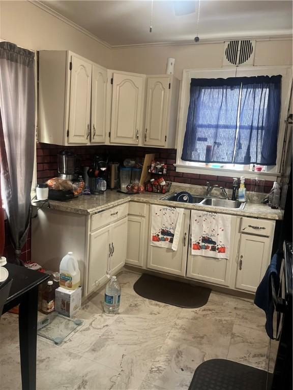 kitchen with tasteful backsplash, sink, white cabinetry, and ornamental molding