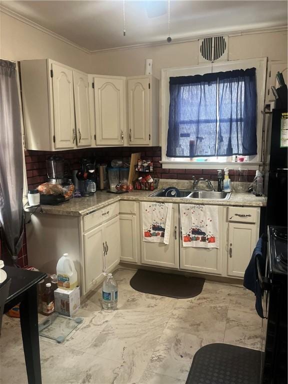 kitchen with ornamental molding, black stove, white cabinets, and sink