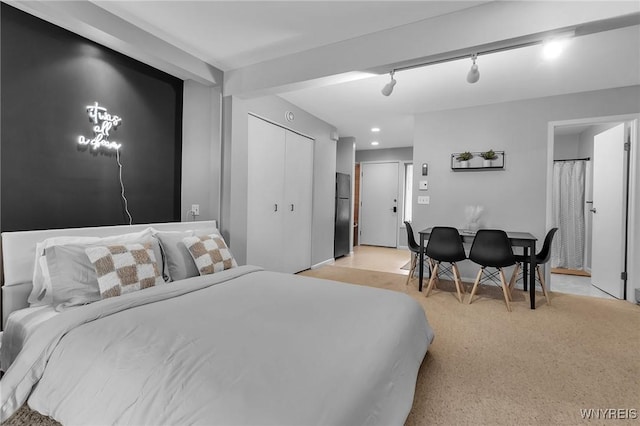 carpeted bedroom with black refrigerator, a closet, and track lighting