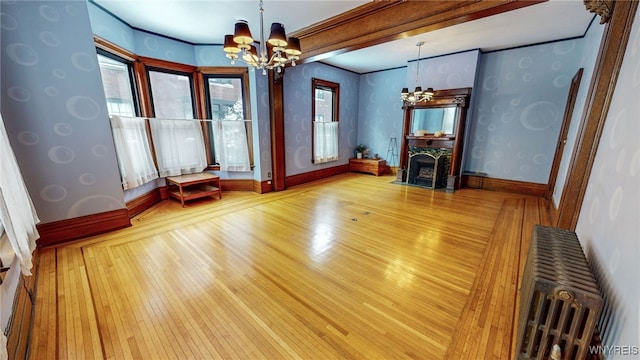 unfurnished living room featuring an inviting chandelier, a wealth of natural light, crown molding, and hardwood / wood-style floors