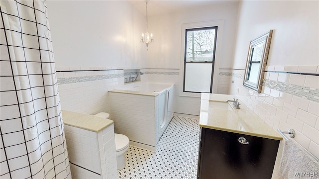 bathroom with toilet, vanity, tile walls, tile patterned flooring, and an inviting chandelier