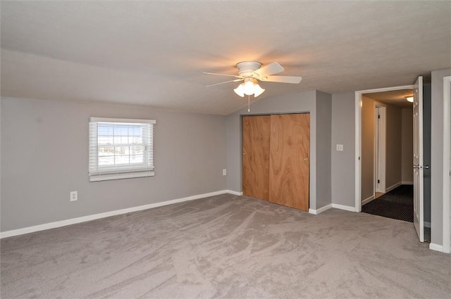 unfurnished bedroom with ceiling fan, a closet, carpet floors, and lofted ceiling