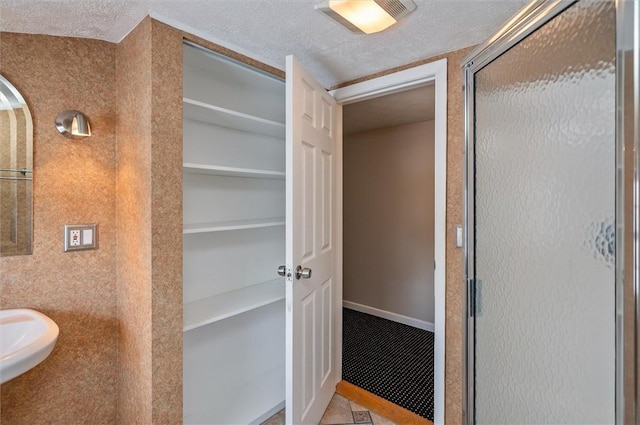 bathroom featuring sink, a textured ceiling, a shower with door, and tile patterned flooring