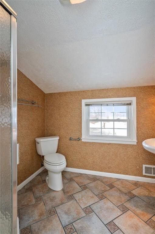 bathroom featuring a textured ceiling, toilet, walk in shower, and vaulted ceiling