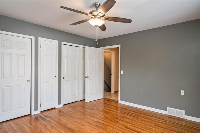 unfurnished bedroom featuring ceiling fan, light hardwood / wood-style flooring, and two closets