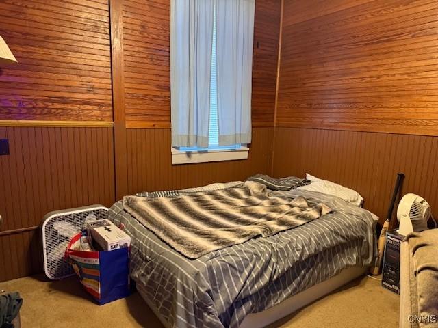 bedroom featuring light colored carpet and wood walls