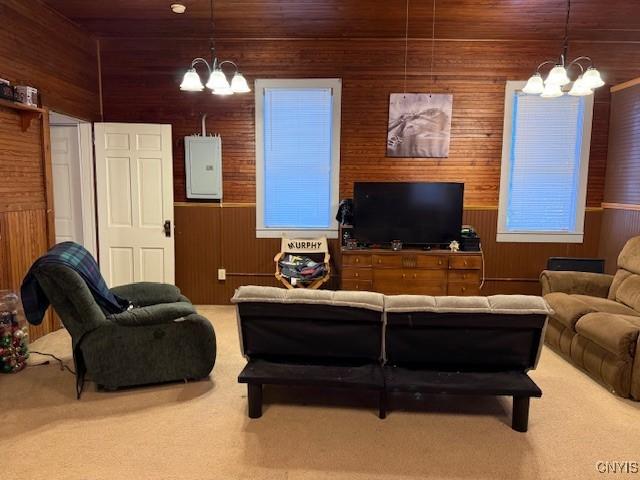 living room with electric panel, carpet flooring, wood walls, and an inviting chandelier