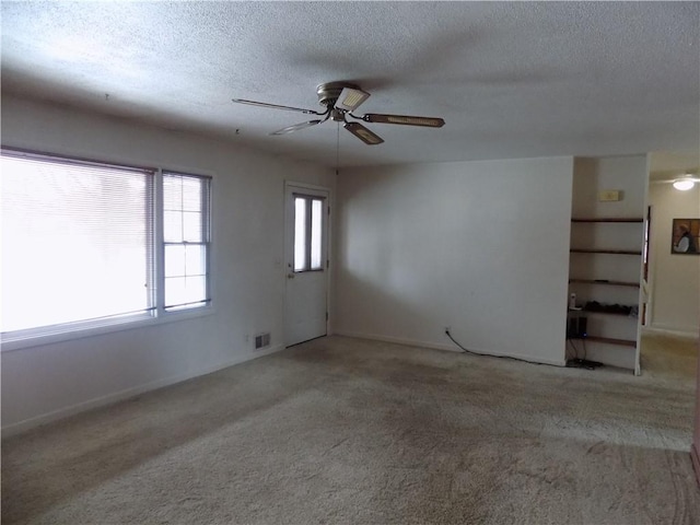 unfurnished room with ceiling fan, a textured ceiling, and light carpet