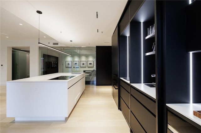 kitchen featuring decorative light fixtures, fridge, black electric stovetop, and an island with sink