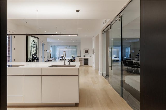 kitchen featuring white cabinets, decorative light fixtures, wine cooler, sink, and light wood-type flooring