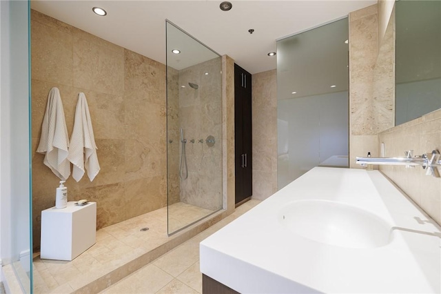 bathroom with tile walls, tile patterned flooring, sink, and a tile shower