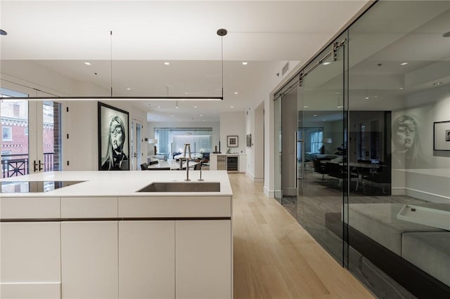 kitchen with light hardwood / wood-style floors, sink, hanging light fixtures, white cabinets, and black electric cooktop