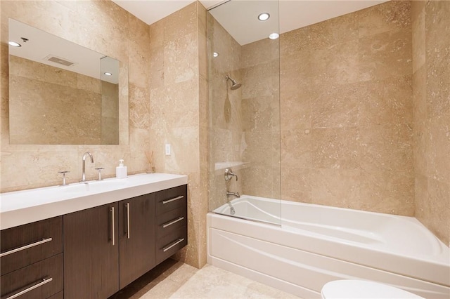 full bathroom featuring toilet, tile walls, vanity, and tiled shower / bath combo