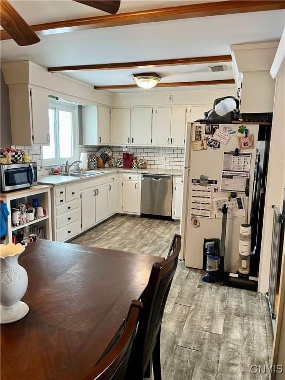 kitchen with white cabinets, stainless steel appliances, decorative backsplash, sink, and light hardwood / wood-style flooring