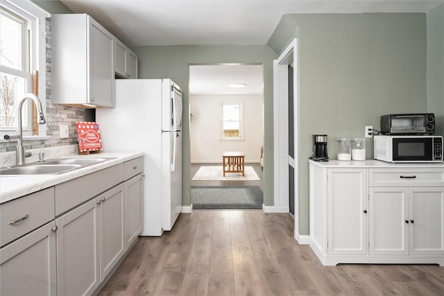 kitchen featuring decorative backsplash, sink, white cabinetry, light wood-type flooring, and white refrigerator