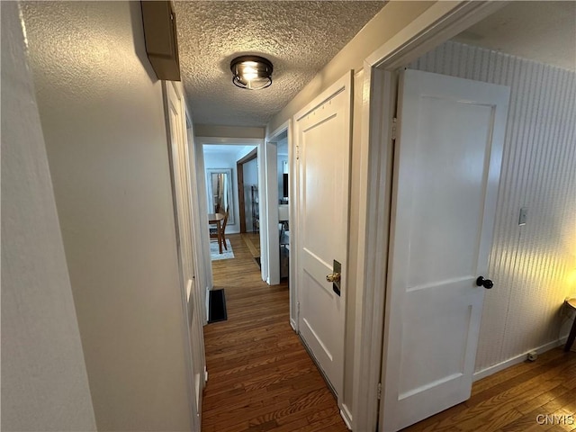 hallway with a textured ceiling and dark hardwood / wood-style flooring