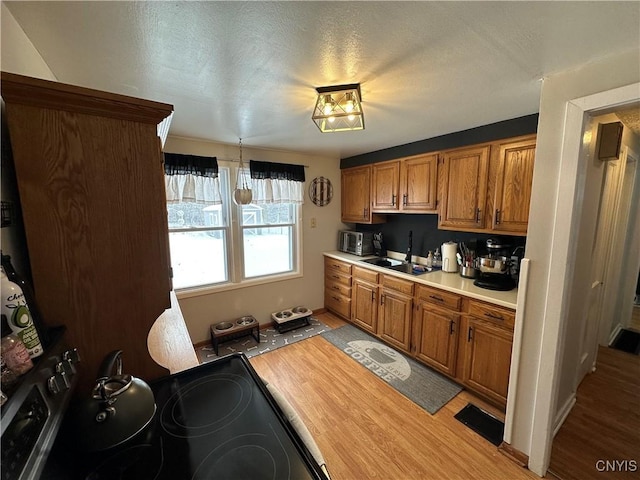 kitchen featuring electric range, hanging light fixtures, a textured ceiling, light hardwood / wood-style flooring, and sink