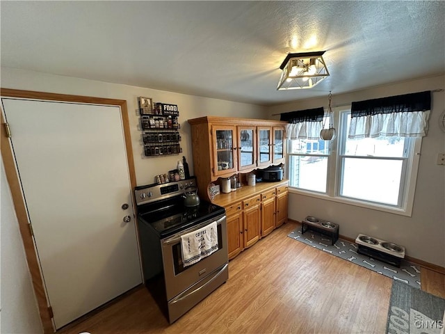 kitchen featuring a textured ceiling, light hardwood / wood-style floors, and stainless steel electric range oven