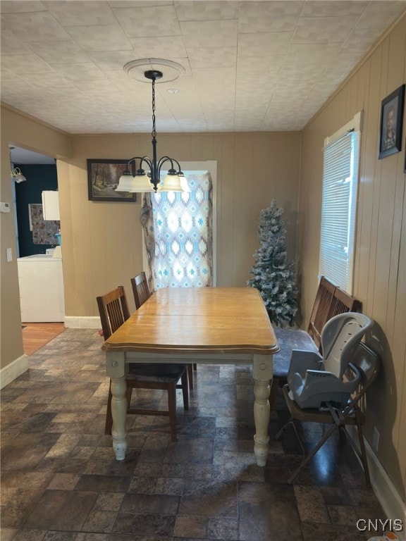 dining area with a chandelier and wood walls