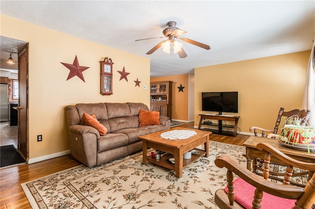 living room with a textured ceiling, ceiling fan, and wood-type flooring