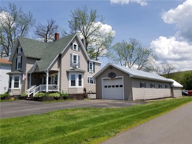 view of front of home with a front yard, a porch, a garage, and an outbuilding