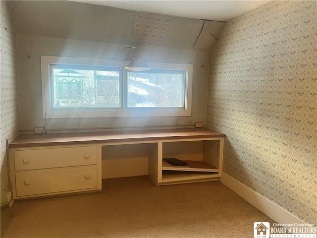 unfurnished office featuring built in desk, light colored carpet, and lofted ceiling