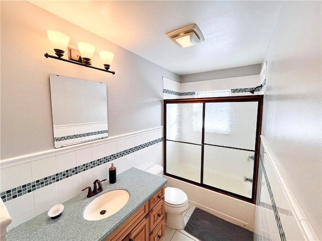 full bathroom featuring shower / bath combination with glass door, tile patterned flooring, vanity, tile walls, and toilet