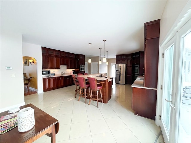 kitchen featuring stainless steel refrigerator with ice dispenser, a kitchen bar, hanging light fixtures, a kitchen island with sink, and light tile patterned flooring