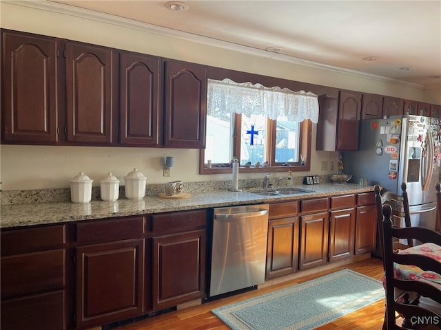 kitchen with appliances with stainless steel finishes, sink, light stone counters, and light hardwood / wood-style floors