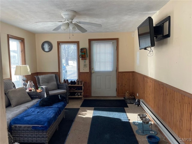 carpeted living room featuring ceiling fan, a baseboard radiator, a textured ceiling, and wooden walls