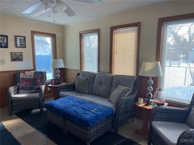 carpeted living room with ceiling fan, plenty of natural light, and wooden walls