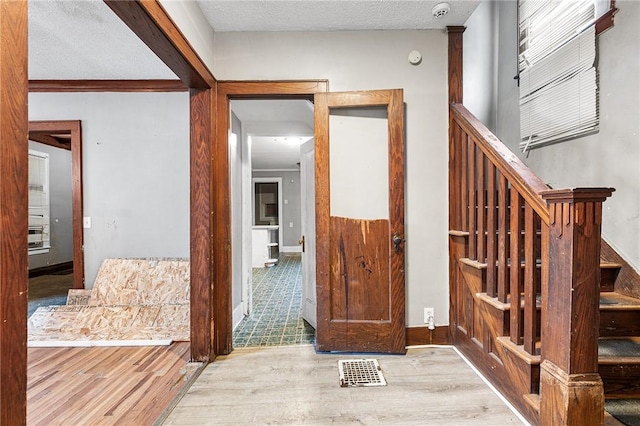 corridor with light hardwood / wood-style floors, a textured ceiling, and crown molding