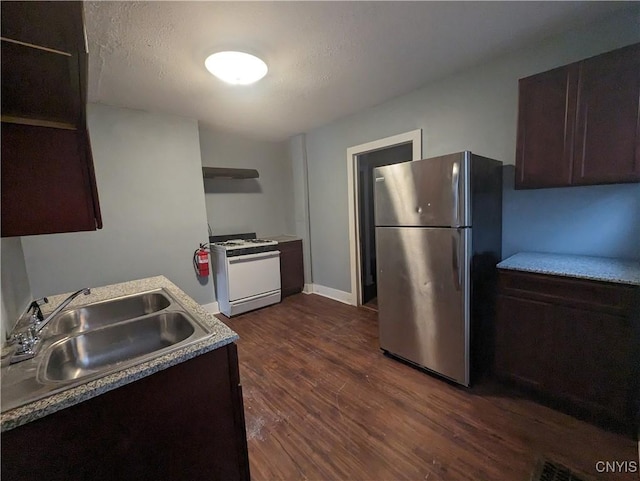 kitchen with a textured ceiling, dark hardwood / wood-style flooring, sink, white gas range oven, and stainless steel refrigerator