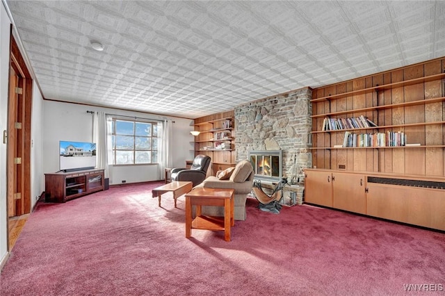 sitting room with carpet floors, built in features, wood walls, and a stone fireplace