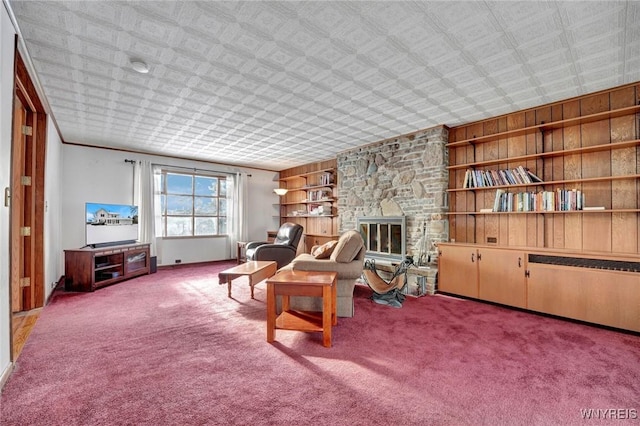 living area with carpet floors, built in shelves, a stone fireplace, and wooden walls