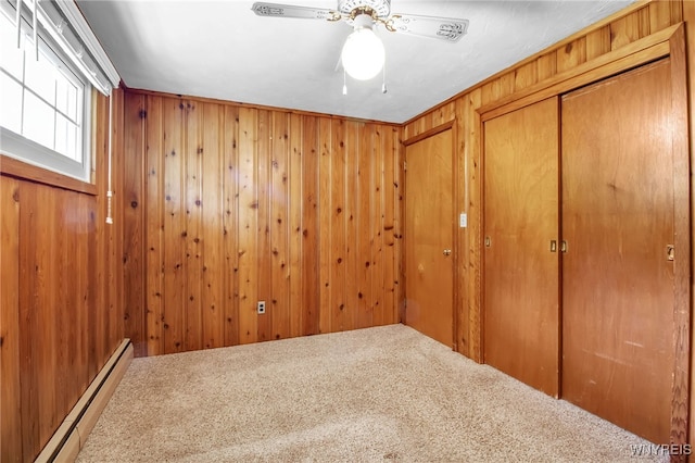 carpeted spare room with ceiling fan, crown molding, wooden walls, and a baseboard radiator