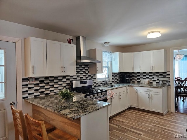 kitchen with kitchen peninsula, wall chimney exhaust hood, stainless steel range with gas cooktop, and white cabinetry