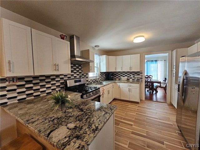 kitchen featuring appliances with stainless steel finishes, wall chimney exhaust hood, white cabinetry, kitchen peninsula, and light stone counters