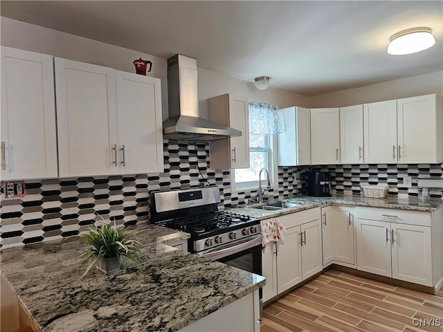 kitchen with white cabinetry, stainless steel gas range oven, wall chimney range hood, light stone countertops, and sink